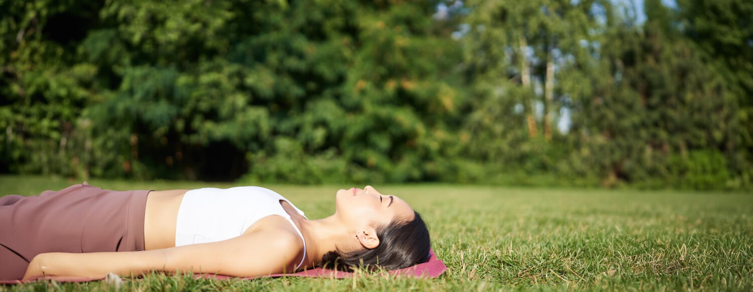 Young fitness girl lying sport mat lawn breathing meditating park sportswear